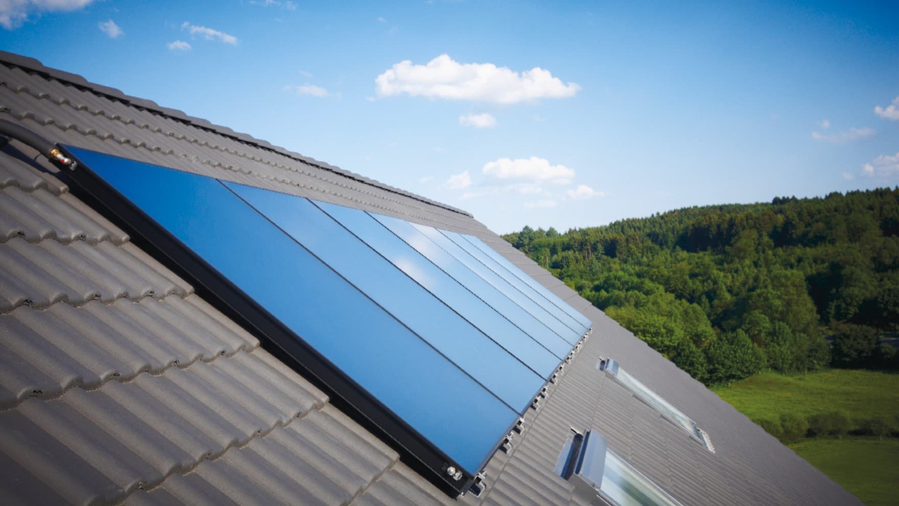 Solarkollektoren auf Hausdach mit Himmel und Wald im Hintergrund