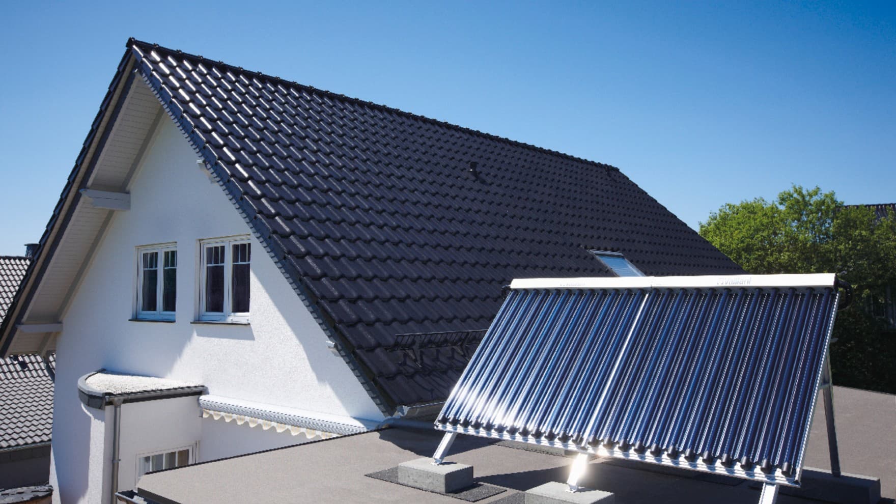 Ein Röhrenkollektor steht vor einem Hausdach auf einer Dachterrasse neben dem Haus.