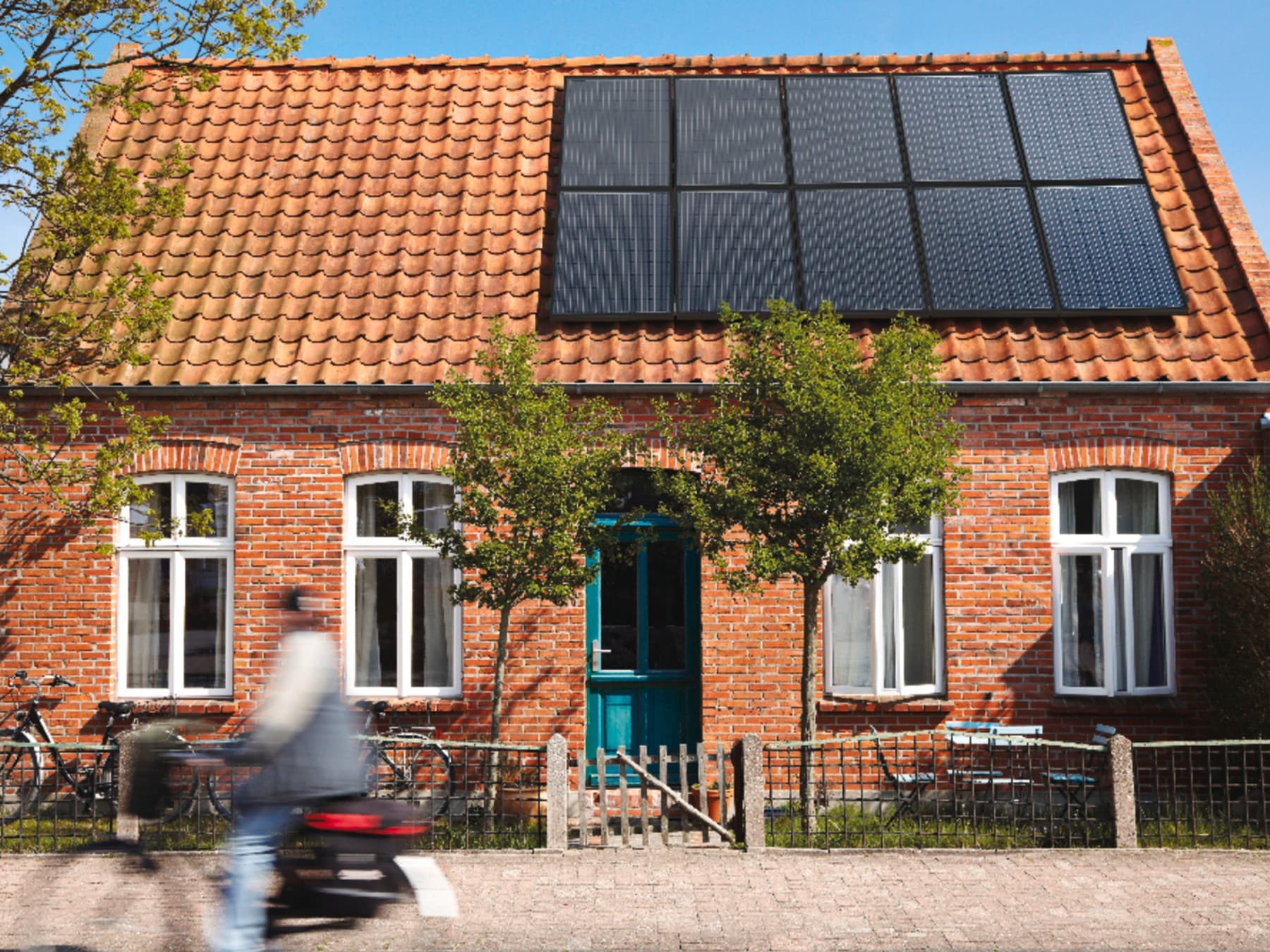 Ein Backsteingebäude mit rot gedecktem Ziegeldach, auf dem sich mehrere Solarpaneele befinden.