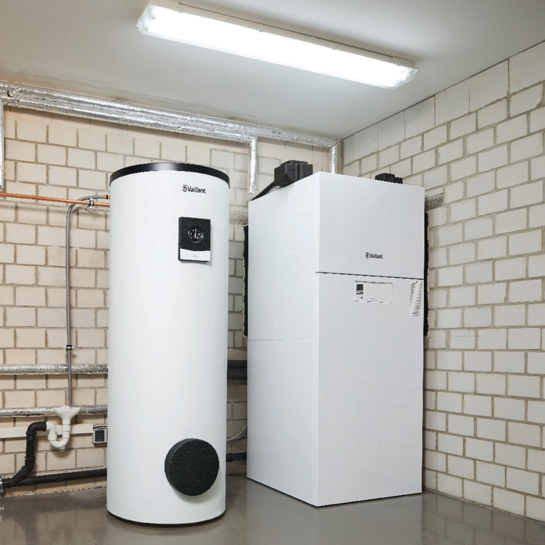 Ein Warmwasserspeicher von Vaillant steht neben einer Vaillant Heizung in einem Kellerraum.