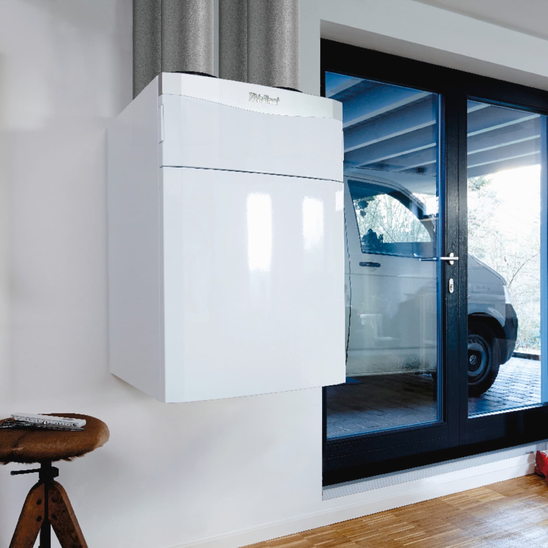Eine Vaillant Lüftungsanlage hängt in einem Flur an der Wand. Daneben sieht man durch eine Glastür den Carport mit geparktem Fahrzeug.