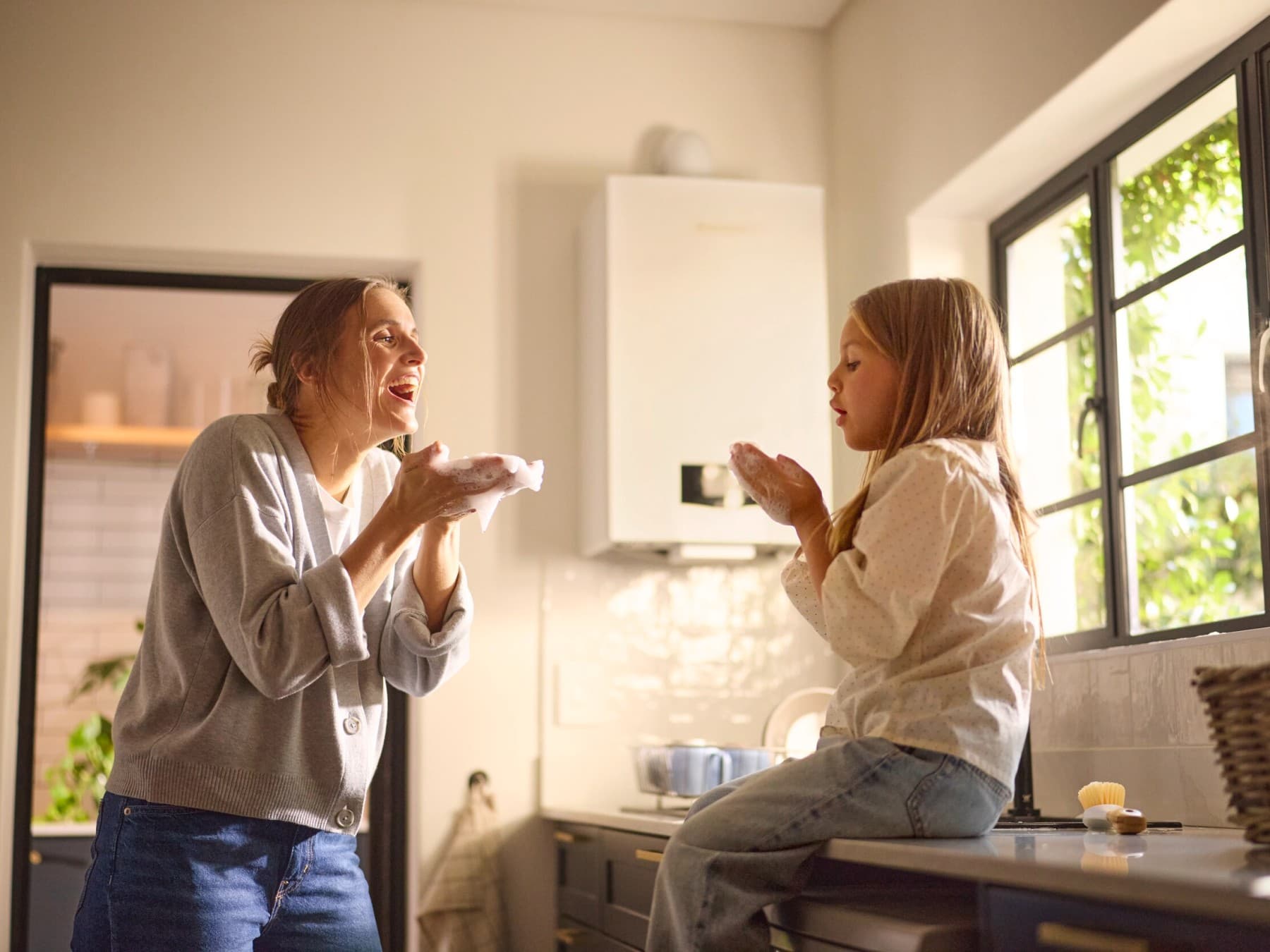 Mutter und Tochter spielen mit Spülschaum in der Küche, im Hintergrund hängt das platzsparende Vaillant Gas-Brennwertgerät ecoTEC plus an der Wand