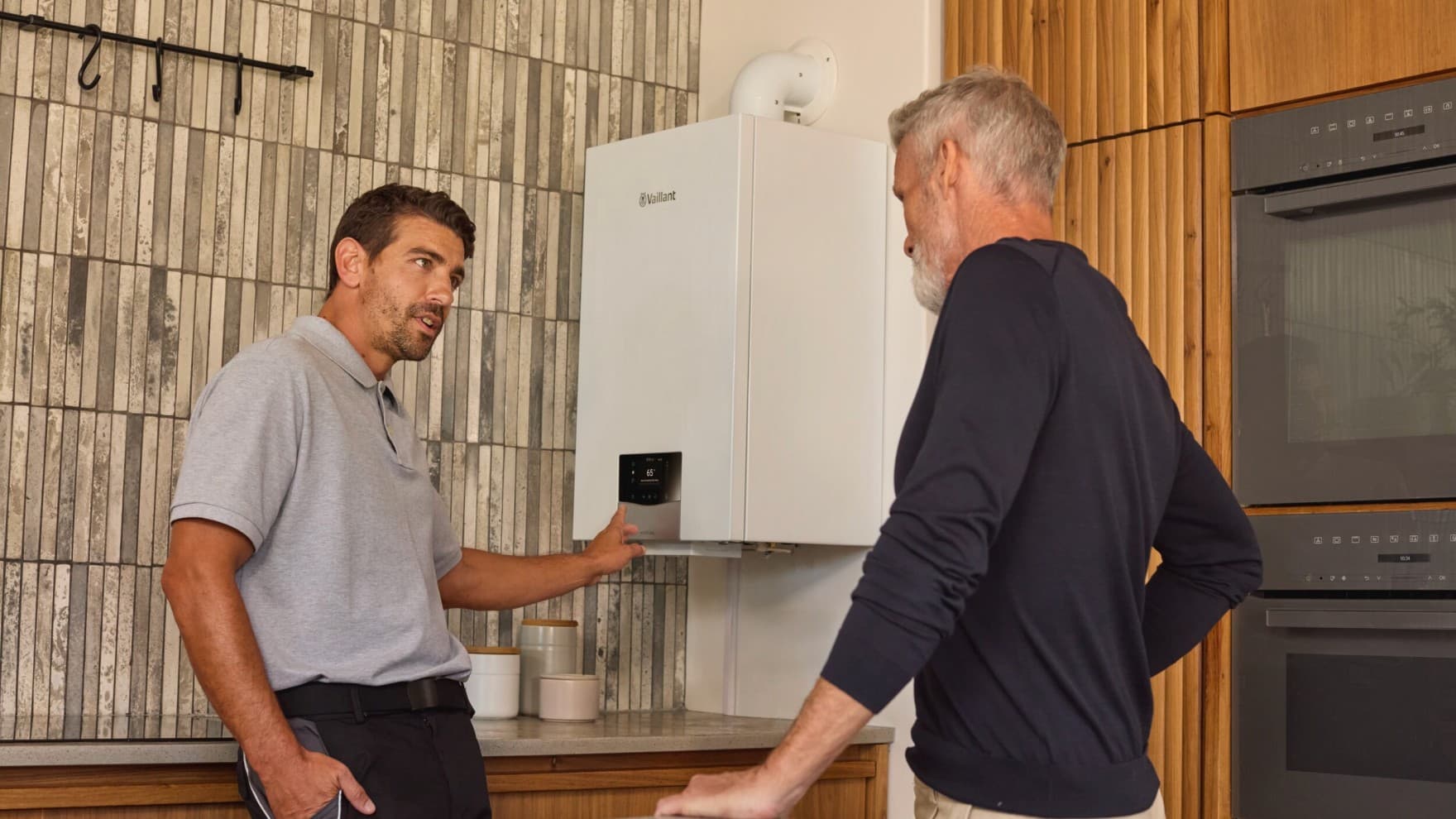 Vaillant Installateur im Dialog mit einem Kunden vor einem wandhängenden Gasgerät