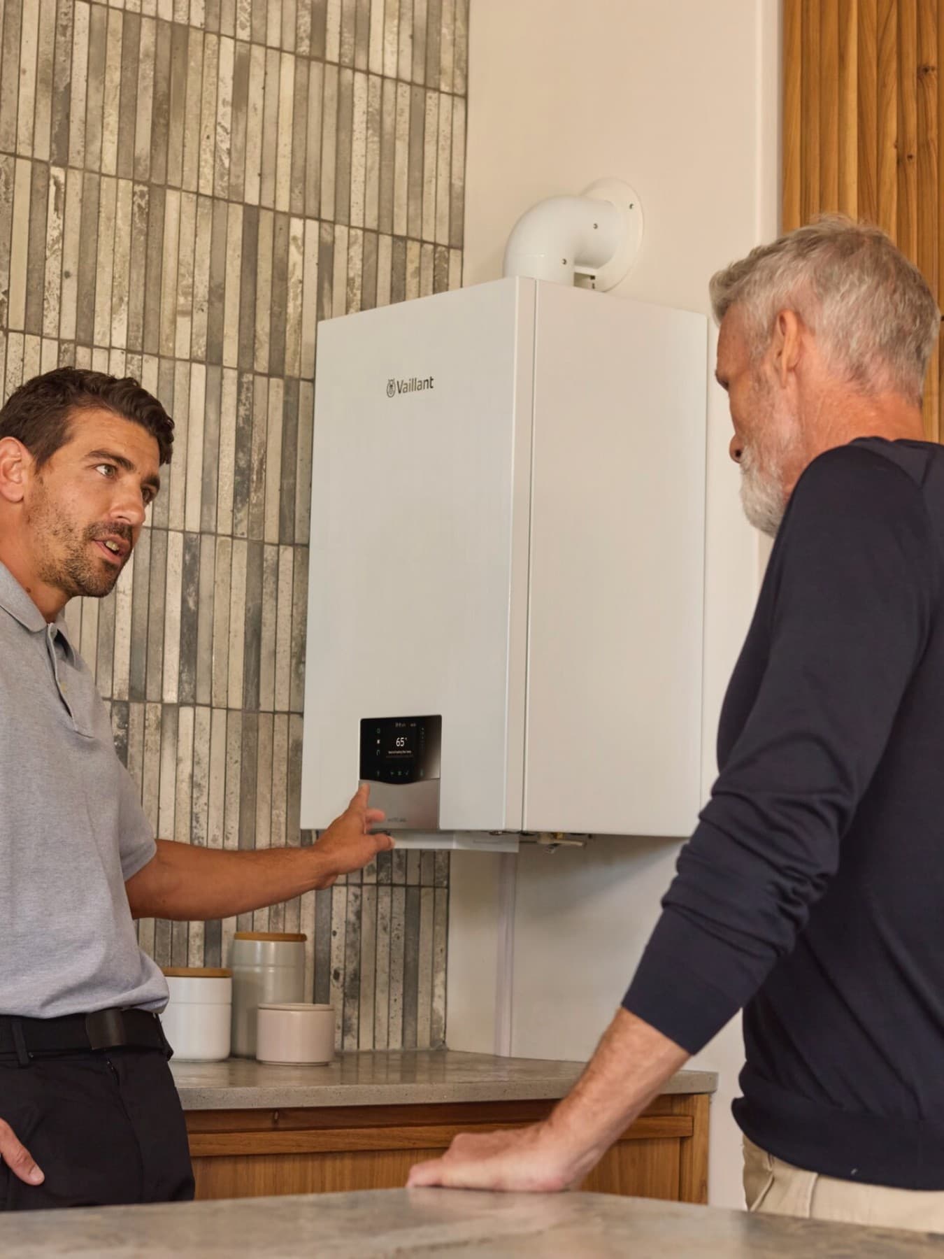 Vaillant Installateur im Dialog mit einem Kunden vor einem wandhängenden Gasgerät