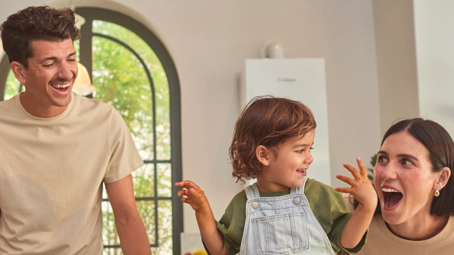 Ein Paar, das mit seinem Kind in der Küche Spaß hat, im Hintergrund ein Gasgerät an der Wand.