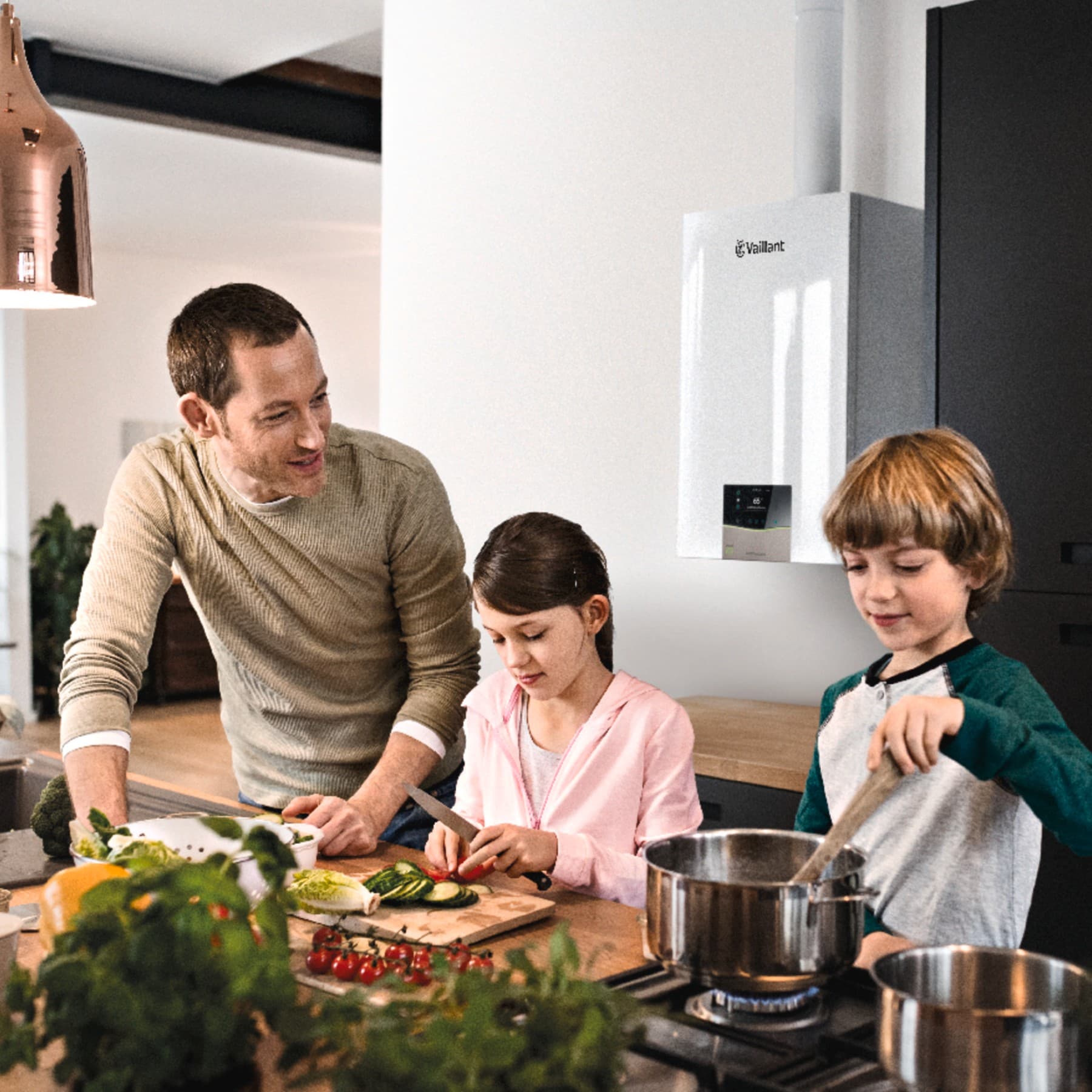 Vater und Kinder beim Kochen in der Küche. Im Hintergrund hängt ein Vaillant Gerät an der Wand