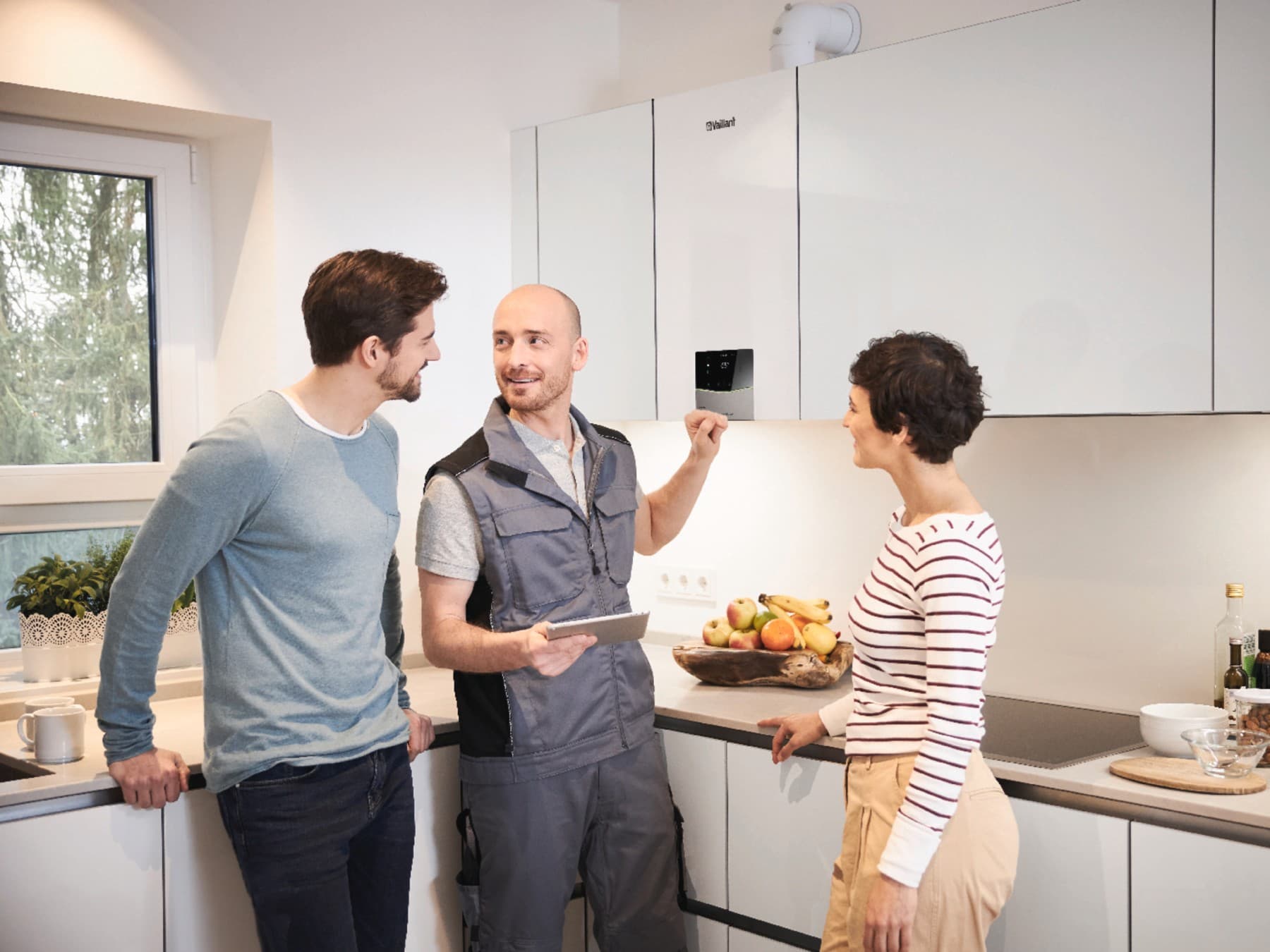 Ein Vaillant Mitarbeiter erklärt einem Mann und einer Frau in einer Küche ihr neues Vaillant Heizgerät.