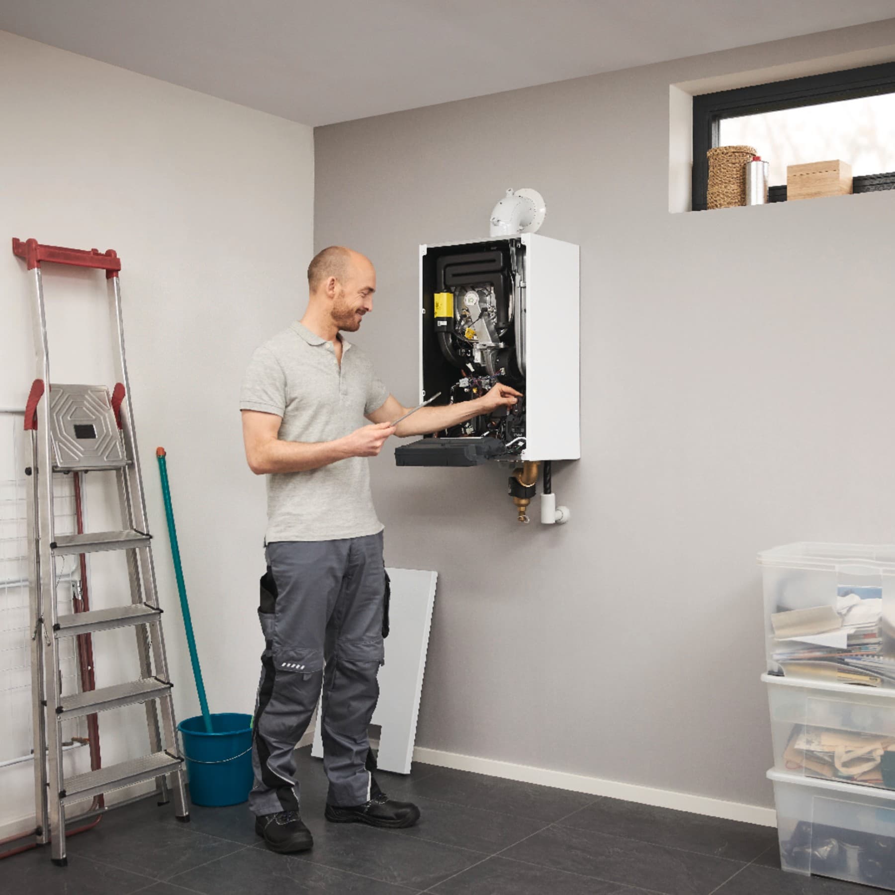 Mann steht im Keller und nimmt Einstellungen am wandhängenden Gas-Brennwertgerät vor.